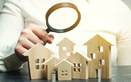 Symbolbild Wohnungsmarktbeobachtung: Arm mit Lupe über Miniaturhäusern