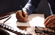 Symbolbild Brandbrief: Hand schreibt Brief auf Schreibtisch