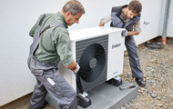 Symbolbild Wärmepumpe: Zwei Monteure installieren eine Luft-Wasser-Wärmepumpe an einem Haus