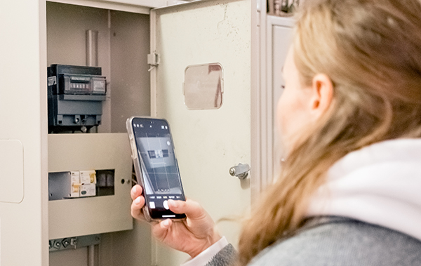 Symbol-Bild Wallbox: Junge Frau lehnt sich an und schaut auf ihr Mobiltelefon, während ihr Elektroauto geladen wird.
