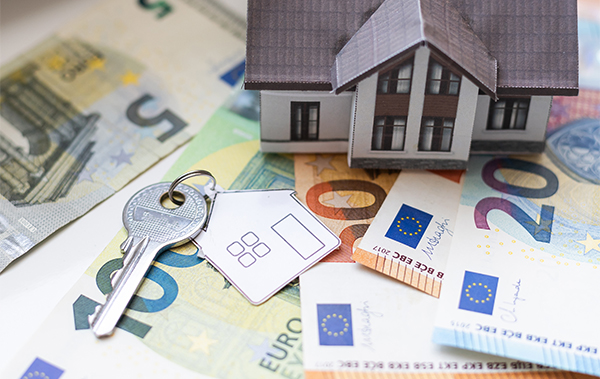 Symbol-Bild für Hausgeldrückstände in der WEG: Miniaturhaus und Hausschlüssel auf einem Untergrund aus Euro-Scheinen