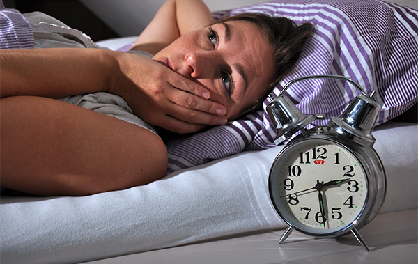 Symbol-Bild für Ängste: Frau liegt nachts im Bett wach, weil sie sich offenbar sorgt. Der Wecker steht auf 2.30 Uhr.