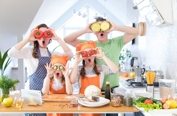 Symbolbild Immobilienerwerb: Familie in Küche albert herum mit Gemüsescheiben als Brille