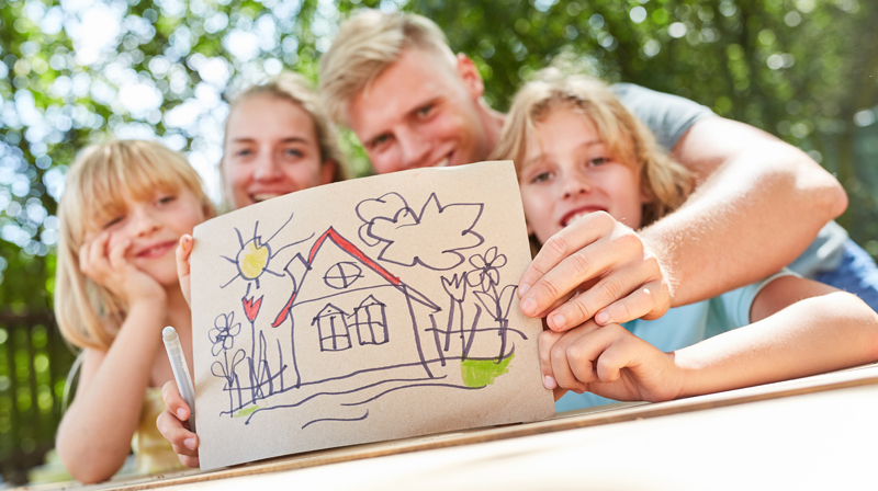 Symbolbild Wunsch nach Wohneigentum: Familie mit der Zeichnung eines Eigenheims