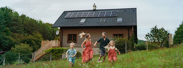 Symbolbild Photovoltaik: laufende, glückliche Familie vor Haus mit Photovoltaik-Anlage